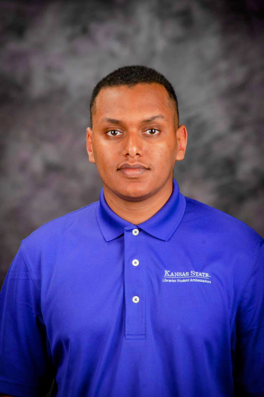 A student in a purple polo smiling for a portrait photo.