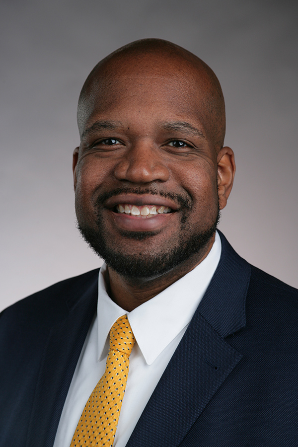 A black man in a suit smiles for a portrait