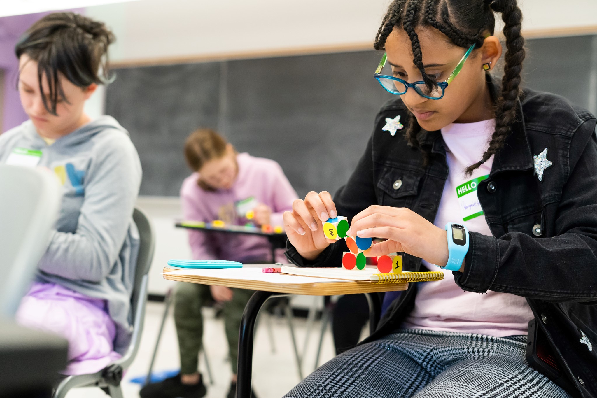 A student sits at a desk and interacts with colorful math-related dice.