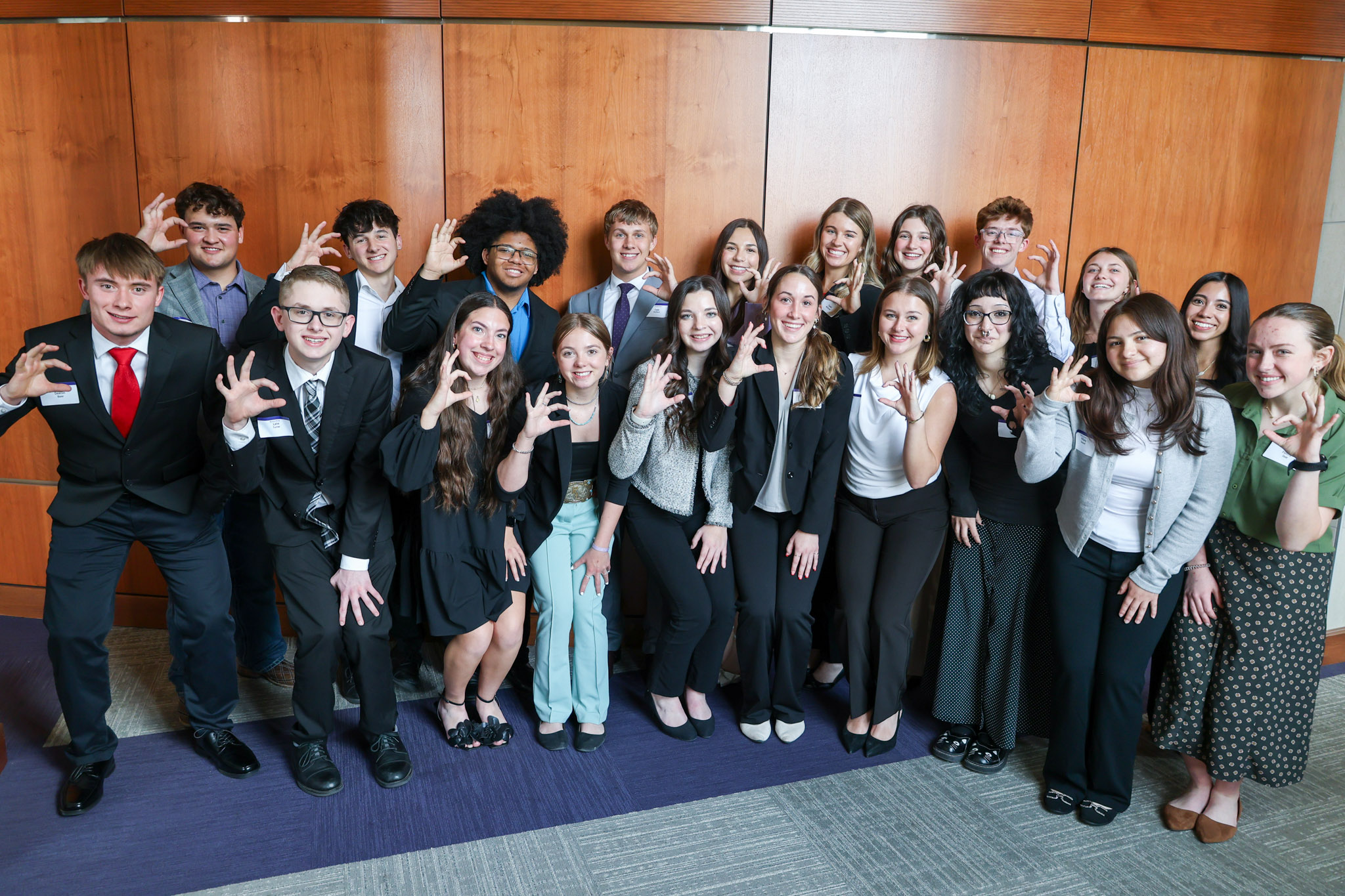A group of students dressed professionally holding up the Wildcat hand sign against a wooden background.