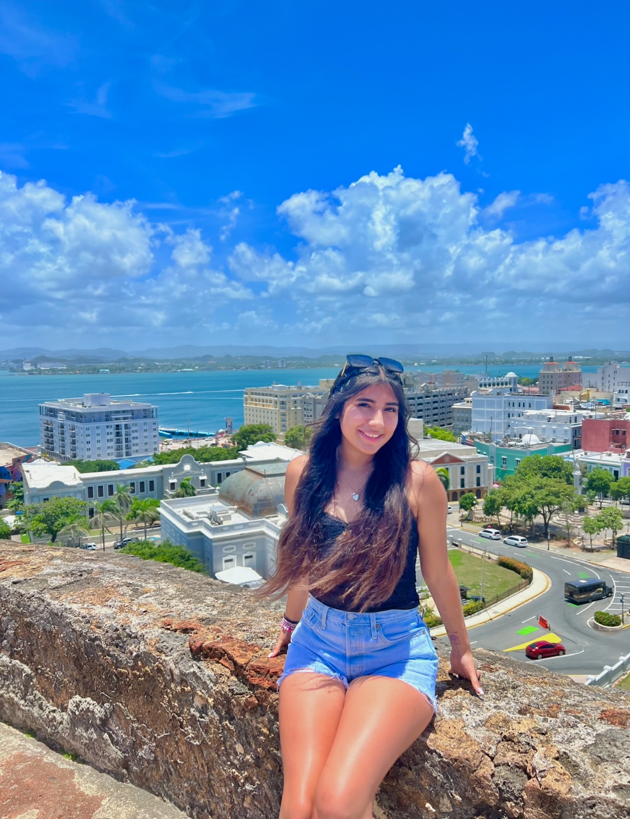 A student sitting on a ledge overlooking a scenic view of water with mountains in the background.