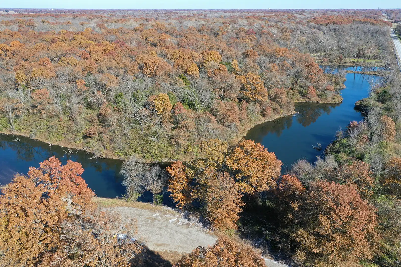 From up above, a dark blue-and-green river winds down and upward underneath an autumn sky. The tree foliage around is orange-ish and amber.