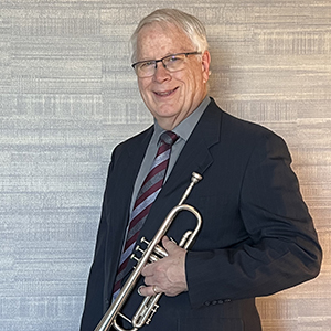 Craig Parker holds a trumpet and smiles for a portrait.