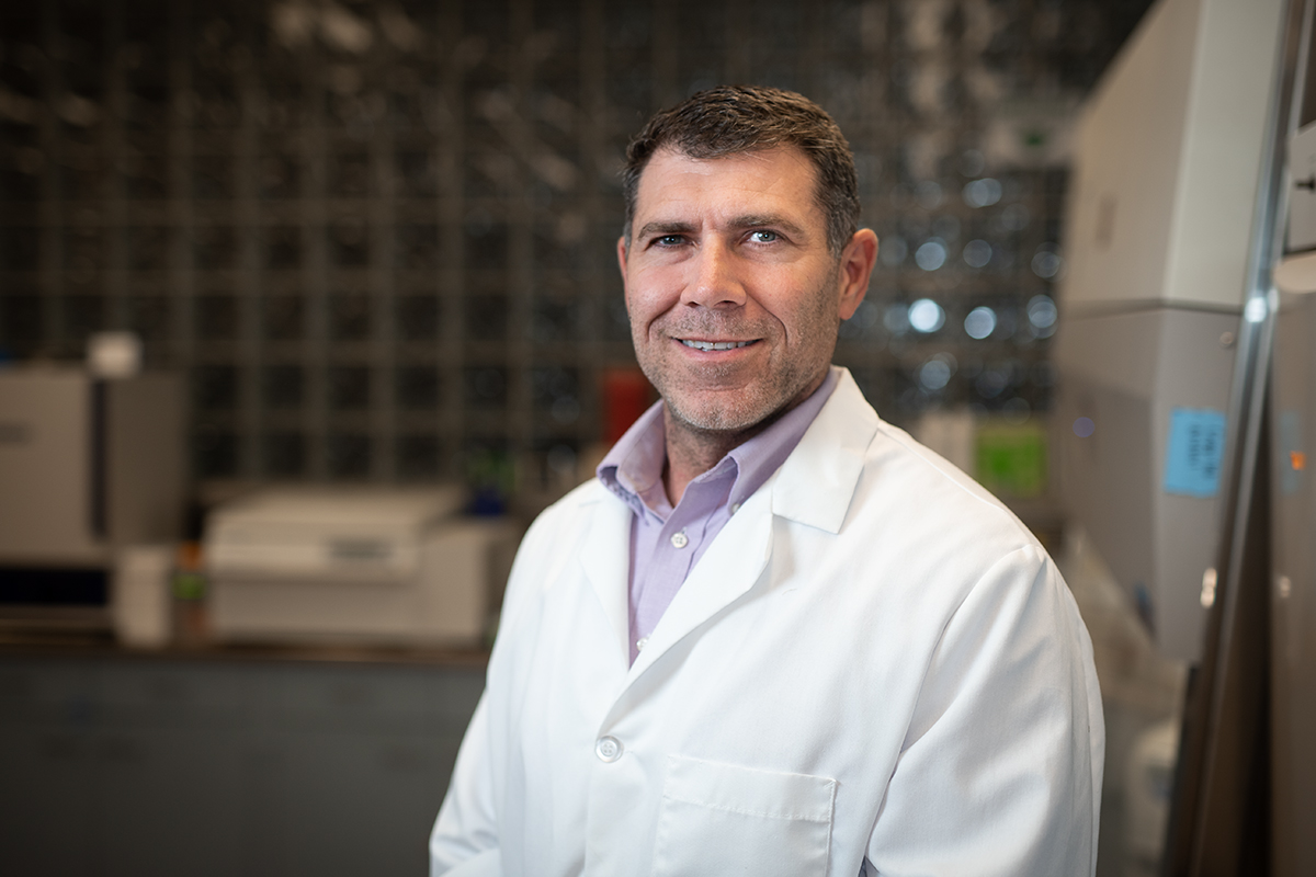 Brad Behnke, wearing a white lab coat, poses for a portrait in a laboratory.