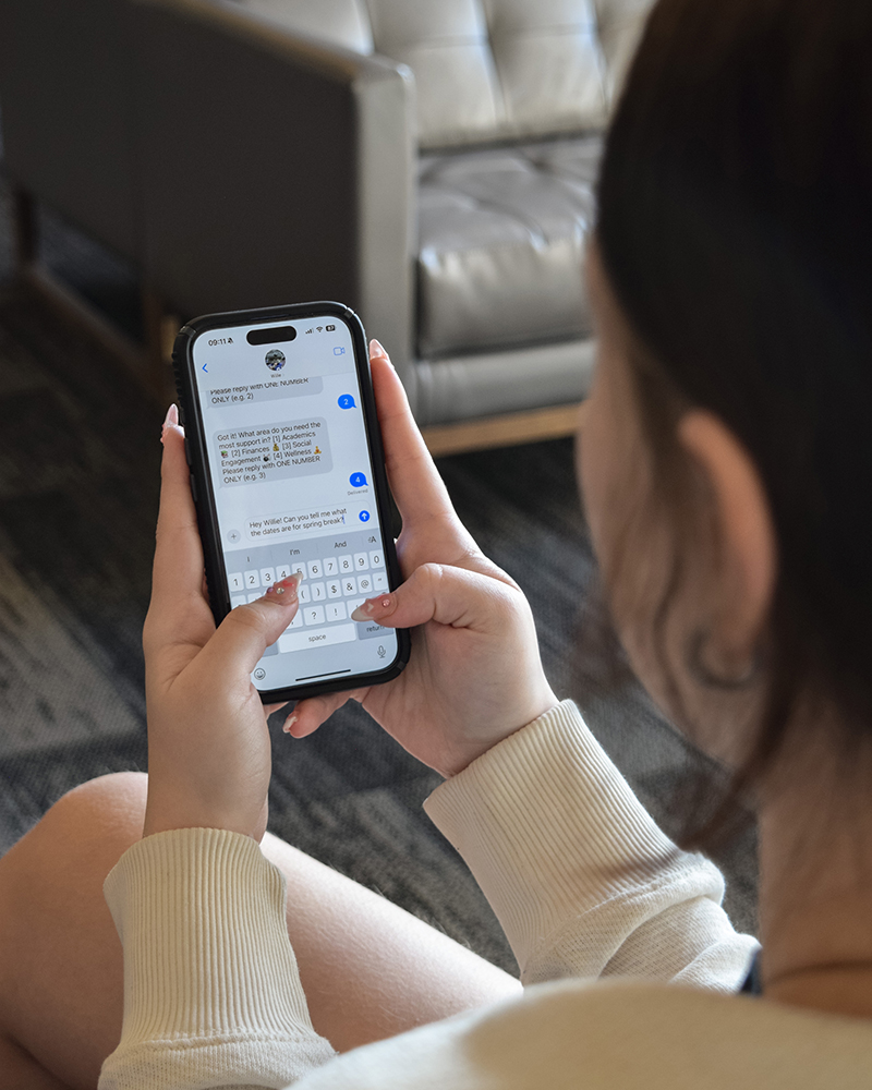 A closeup of a phone screen shows a student texting and having a conversation with a virtual assistant named Willie.