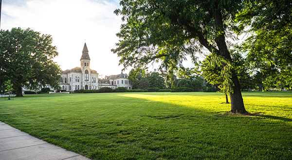 A tall limestone tower stands at the top of a slightly sloped lawn of green grass and trees.