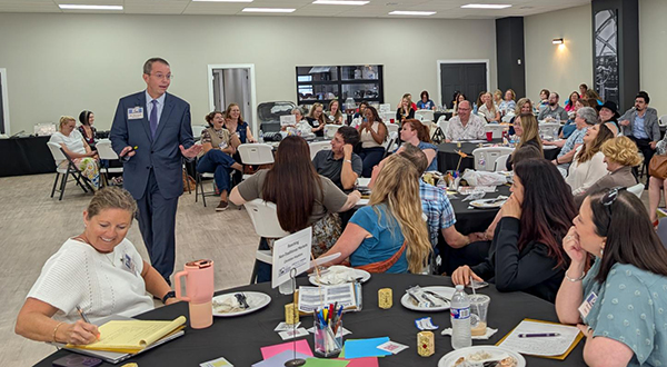 A man in a suit walks among several tables of audience members as he presents about rural business development.