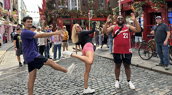 On a colorful Ireland street, three college students pose as the letters K, S and U.