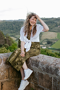 Alexa Murray A young woman sitting on a ledge with a scenic background of green trees and fields.