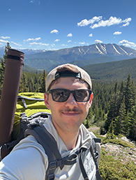 Brayden Shumaker A selfie of a young man outdoors with a mountain behind him.