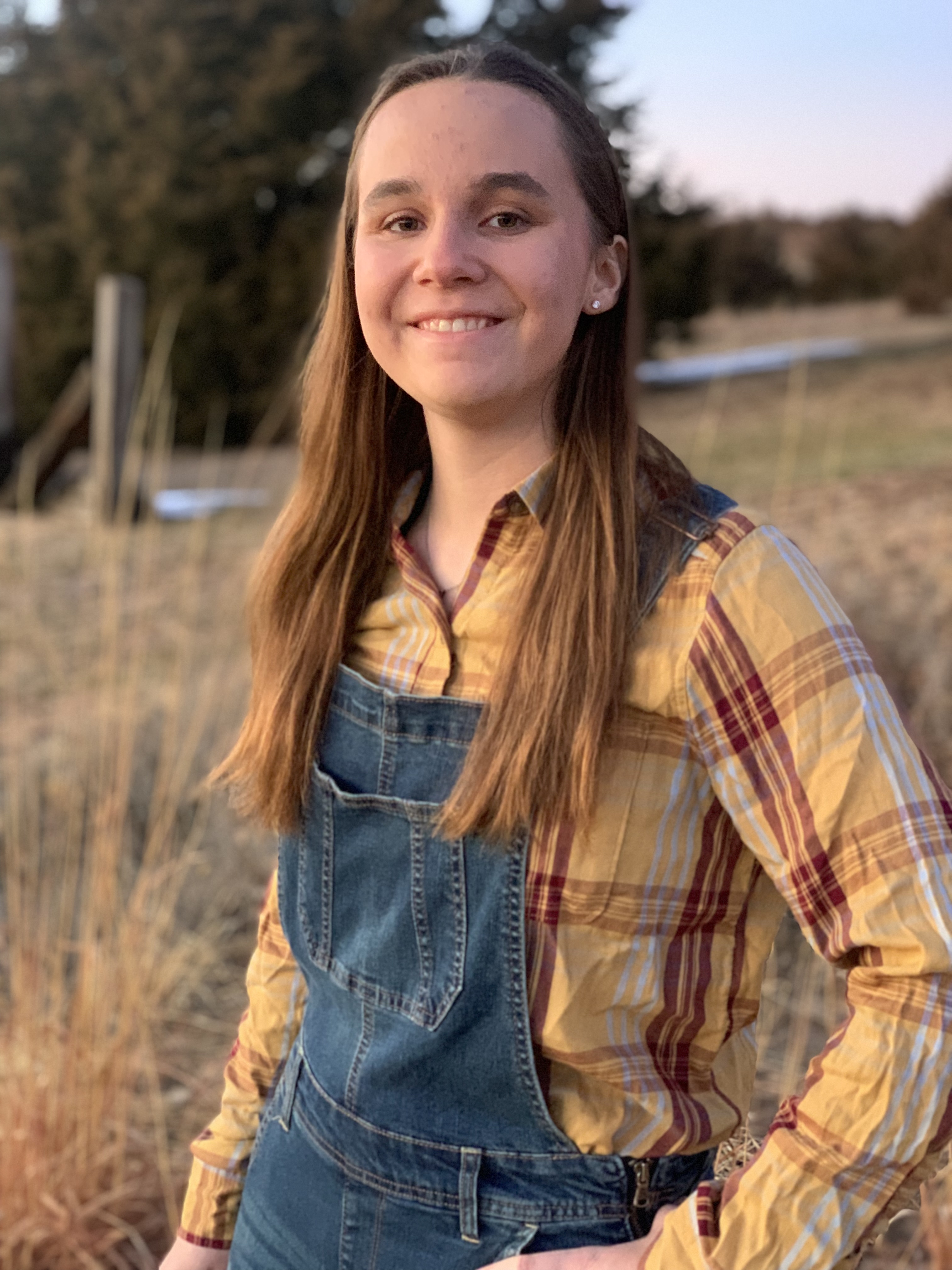 Helen Winters A young woman in a plaid shirt and overalls in a field.