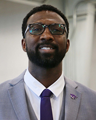 Tysen Pina, wearing glasses and silver suit, stands in a hangar and poses for a portrait.