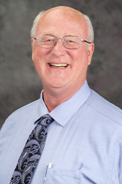 A man in a light blue shirt smiles for a portrait.