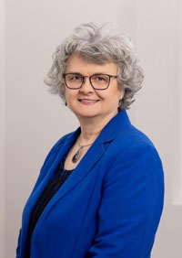 Kara Bell-Fiske wears a royal blue blazer with a navy blue shirt and smiles for a portrait against a white wall.