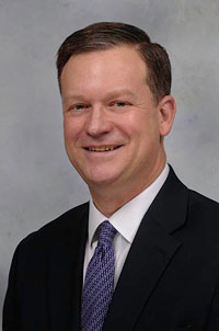 Dan Moser wearing a black suit smiles for portrait.