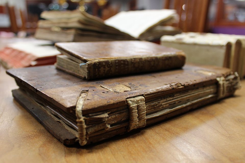 An image of old books on a wooden table shows their old leather bindings.