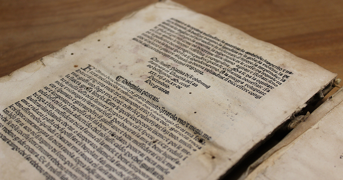 A 15th-century book, written in Latin, lies open on a wooden table.