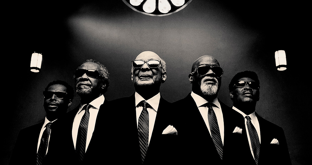 Black and white photo of musical group all wearing sunglasses and suits