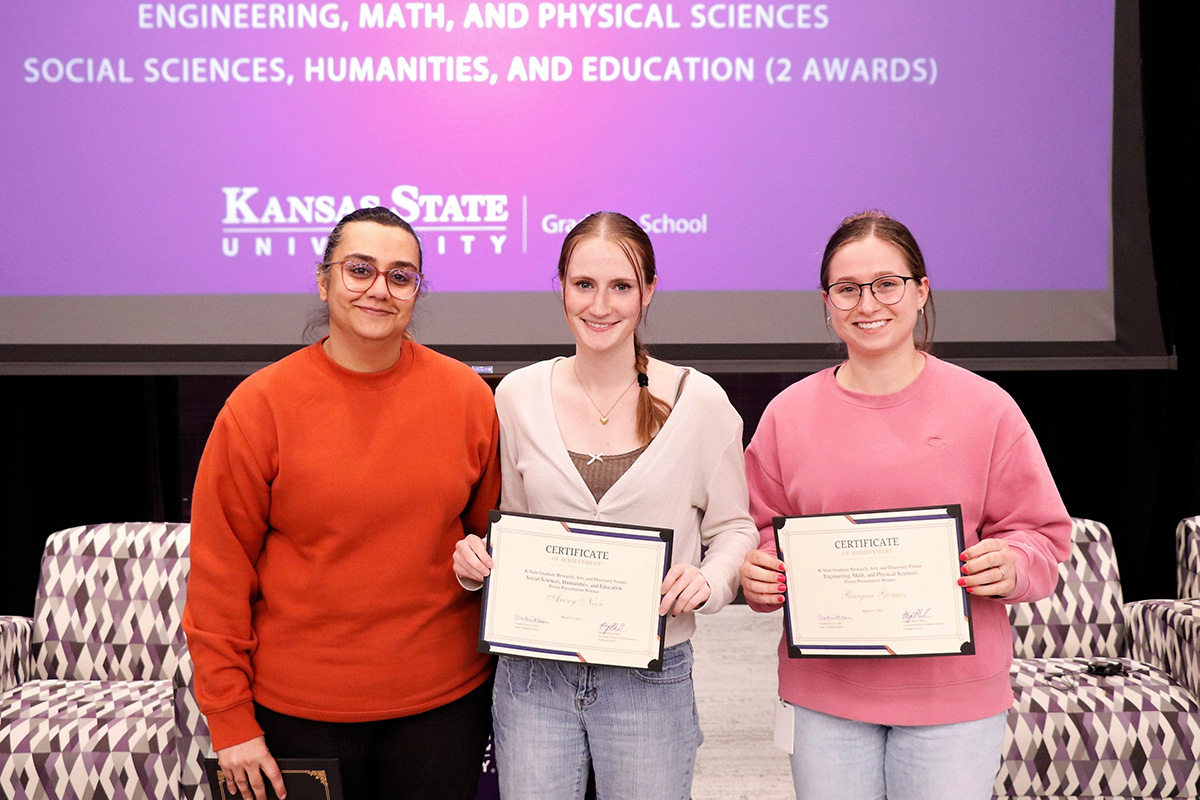 Three women standing in front of a purple screen, two holding certificates