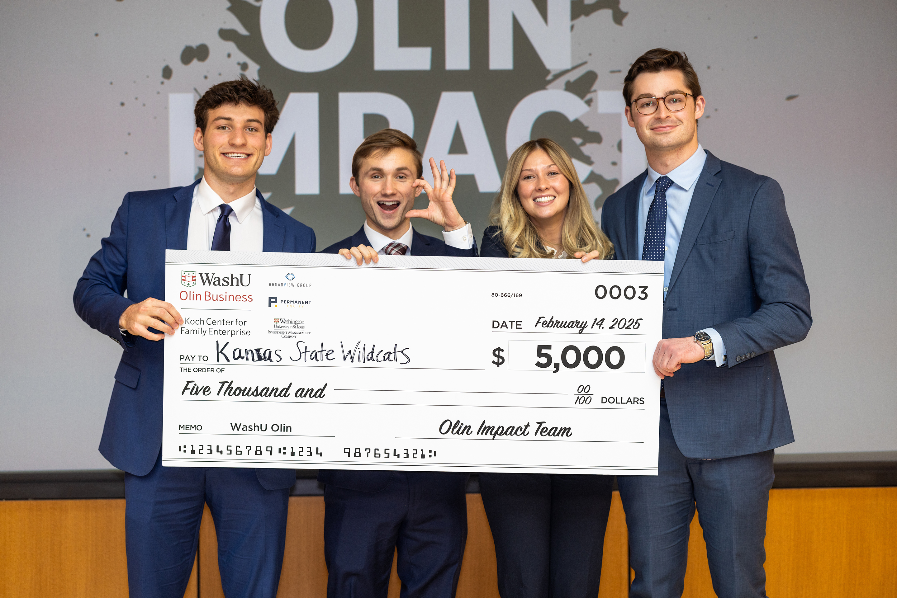 Four students in business suits holding a big check.