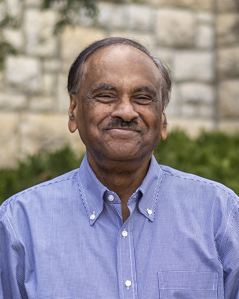 A man in a purple checkered shirt smiles for a portrait.