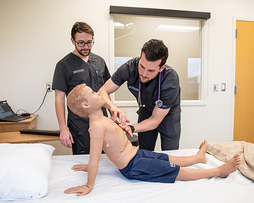 Michael Loree, left, and Grayson Bingham practice their examination skills on "Hal Jr.," an advanced patient simulator.
