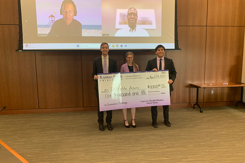 Three students in suits with a large award check.