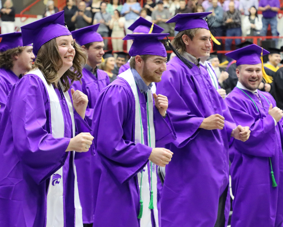 Several graduates in purple caps and gowns do the Wabash, K-State's tradition of rocking back and forth to the unofficial school song "Wabash Cannonball."