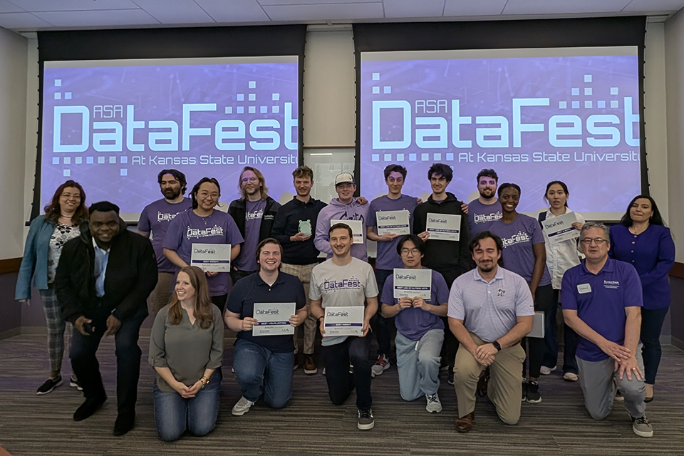 In front of two large screens that say "DataFest," a group of students poses for a group portrait while holding certificates.