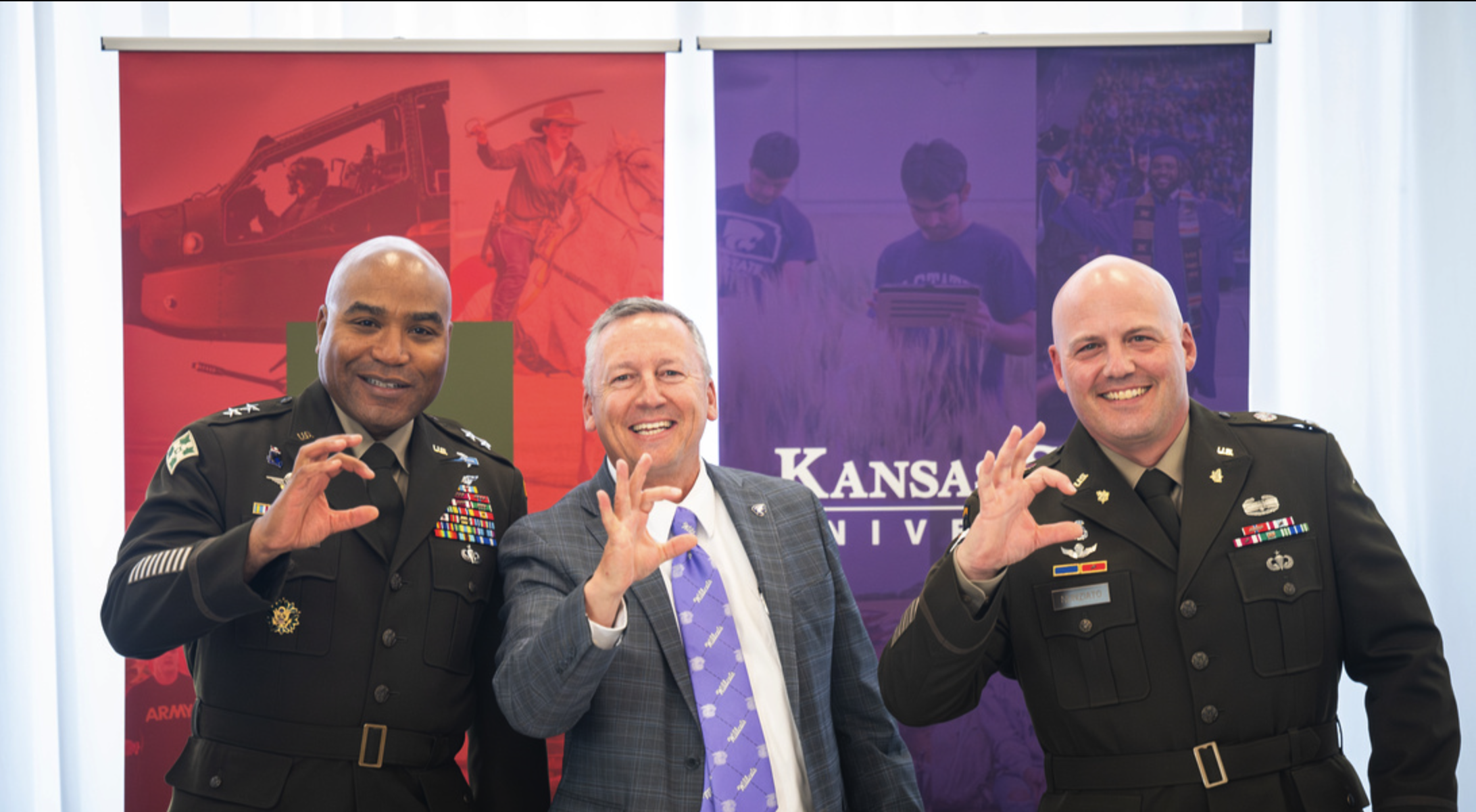 Three men, two in army uniforms, giving the Wildcat hand symbol.