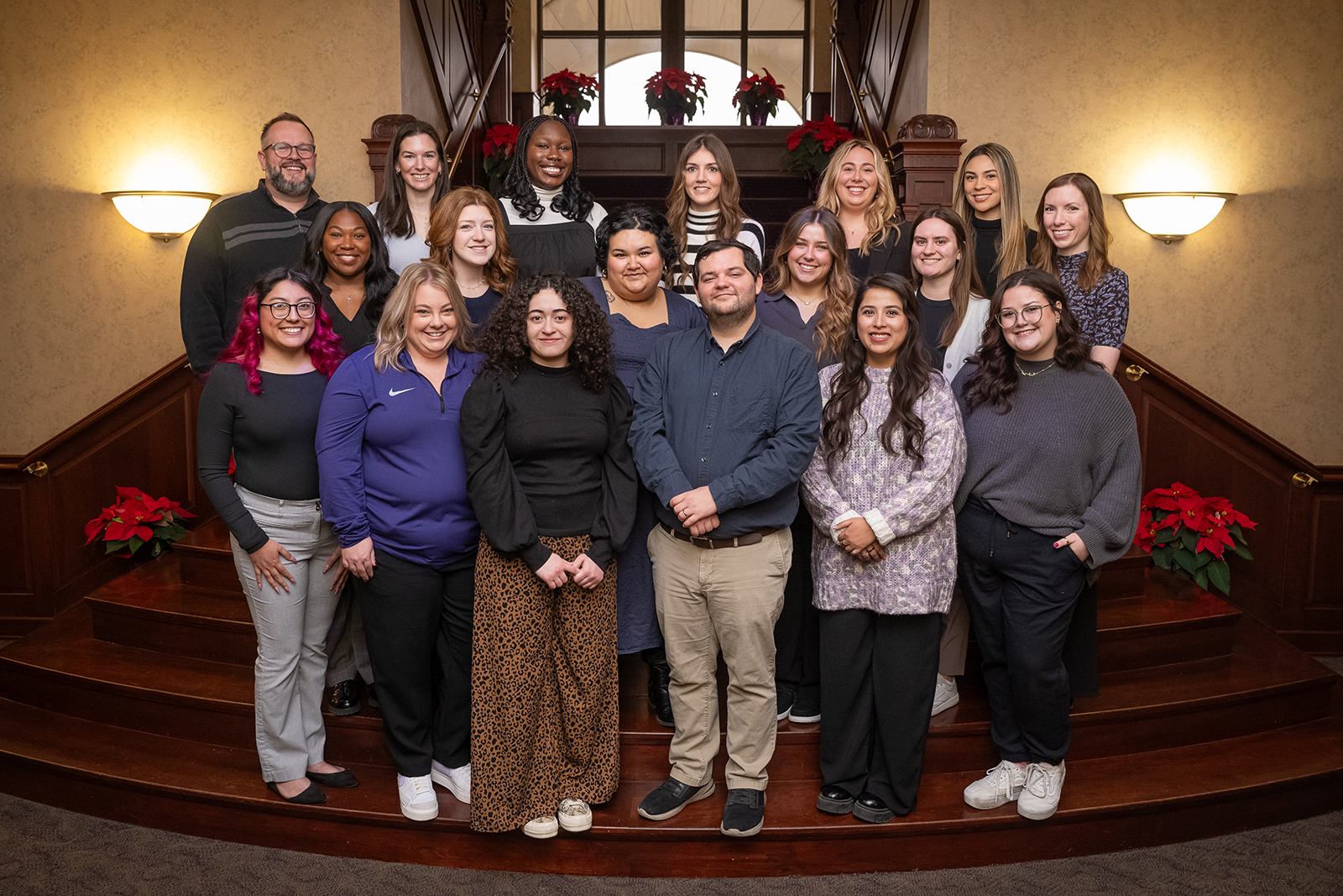 A group of several high school career advisers poses for a group portrait indoors. They are standing in rows on an wide, ornate wooden staircase.