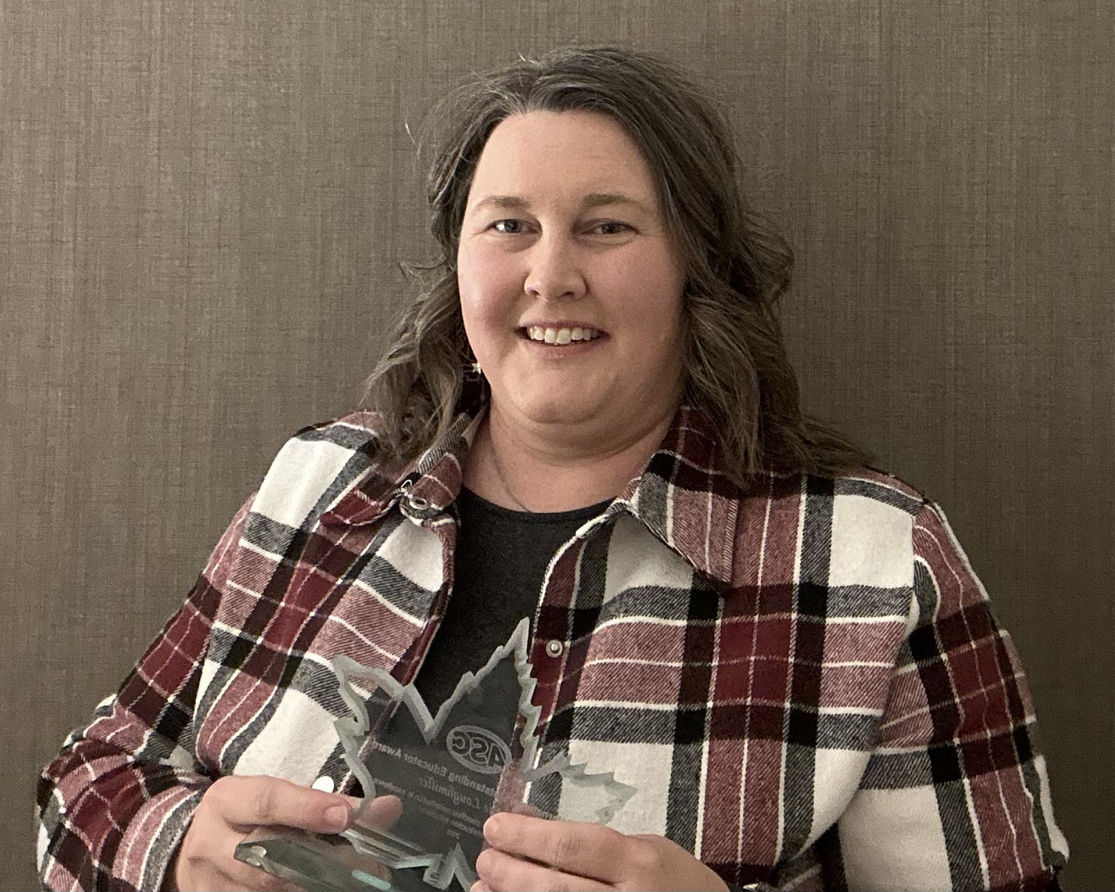 A professor in a red, black and white plaid flannel holds a glass award in the shape of a maple leaf.