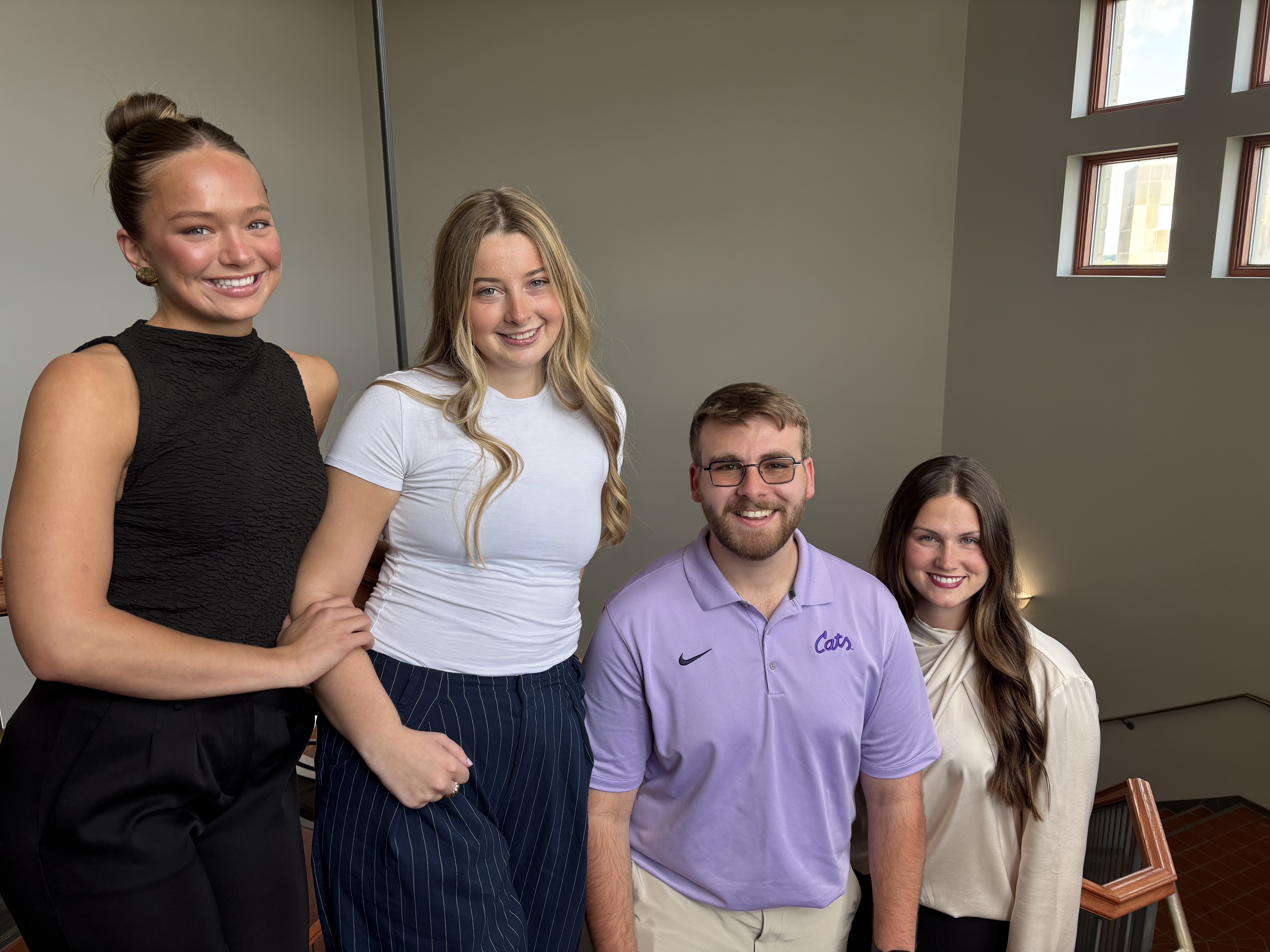 Four students stand in a stairwell and smile for a photo.