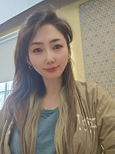 Woman with long brown hair and a blue shirt with tan jacket smiles for a selfie. 