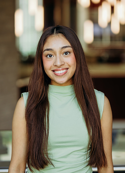 A young woman with brown hair and a light green blouse smiling for a portrait photo.