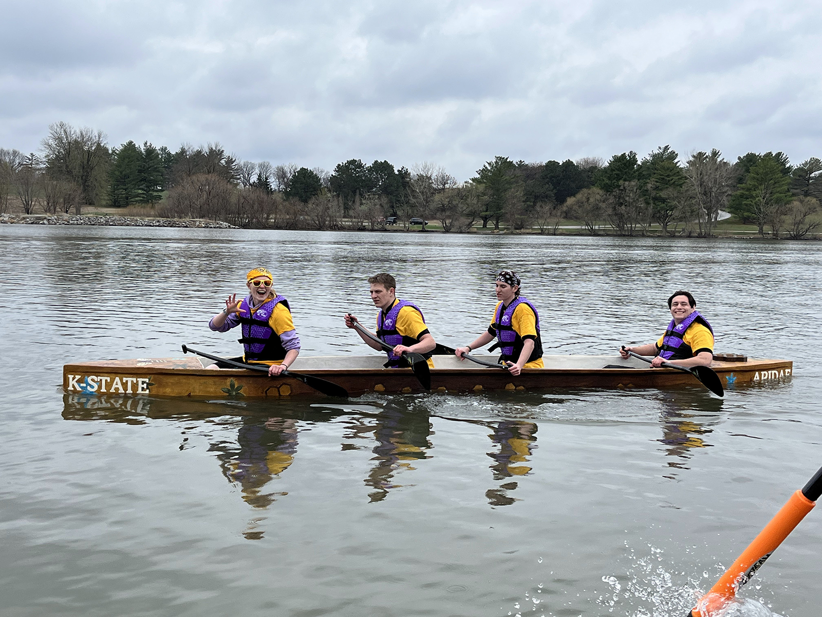 Four students sit and row inside a yellowish canoe made out of concrete.