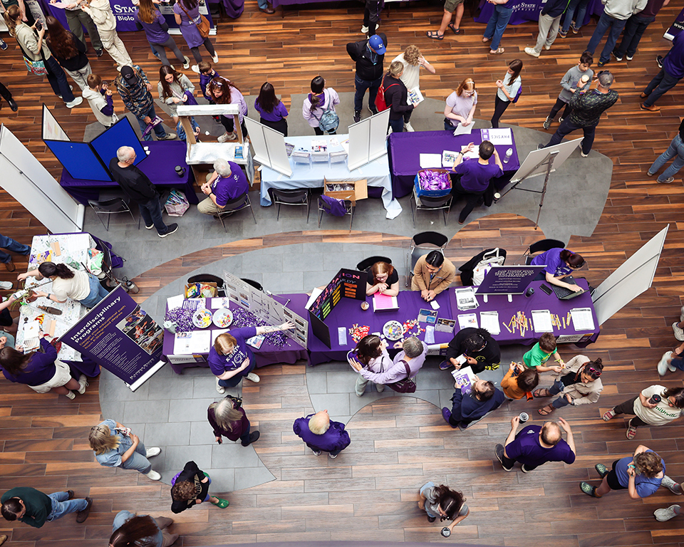 An overhead shot shows several people browsing booths at an information fair in the K-State Student Union during K-State's Open House.
