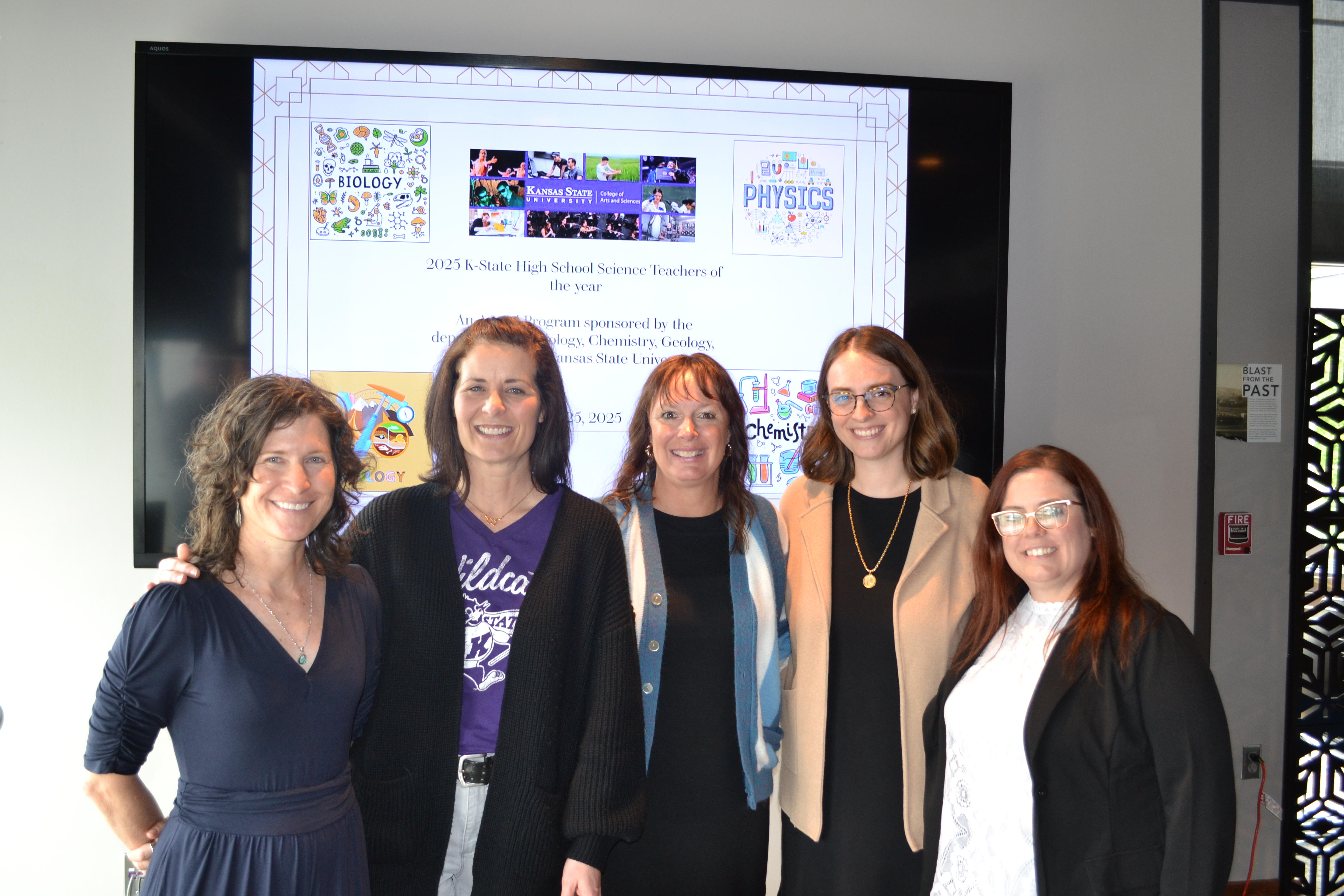 A group of five high school science teachers pose for a group photo in front a classroom projector screen.