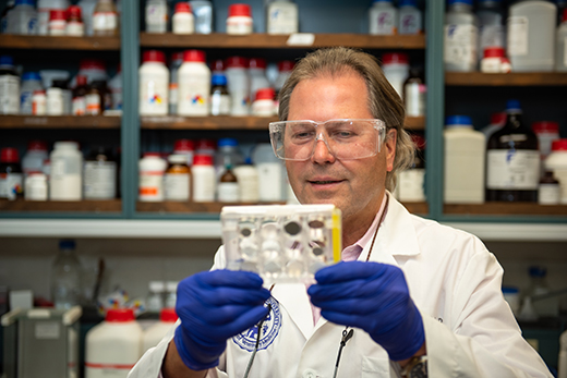 Juergen Richt A man in a white lab coat and safety glasses looking at a sample