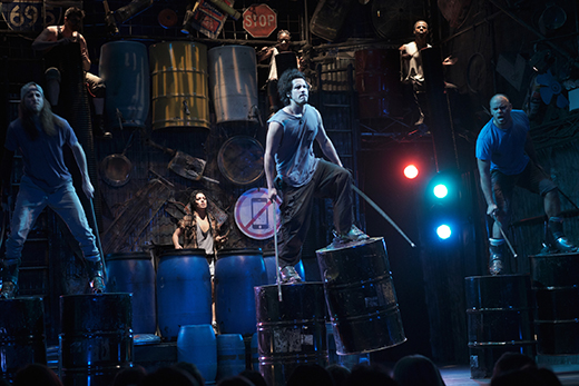 STOMP A diverse group of individuals performing on stage, energetically playing drums in a vibrant atmosphere.