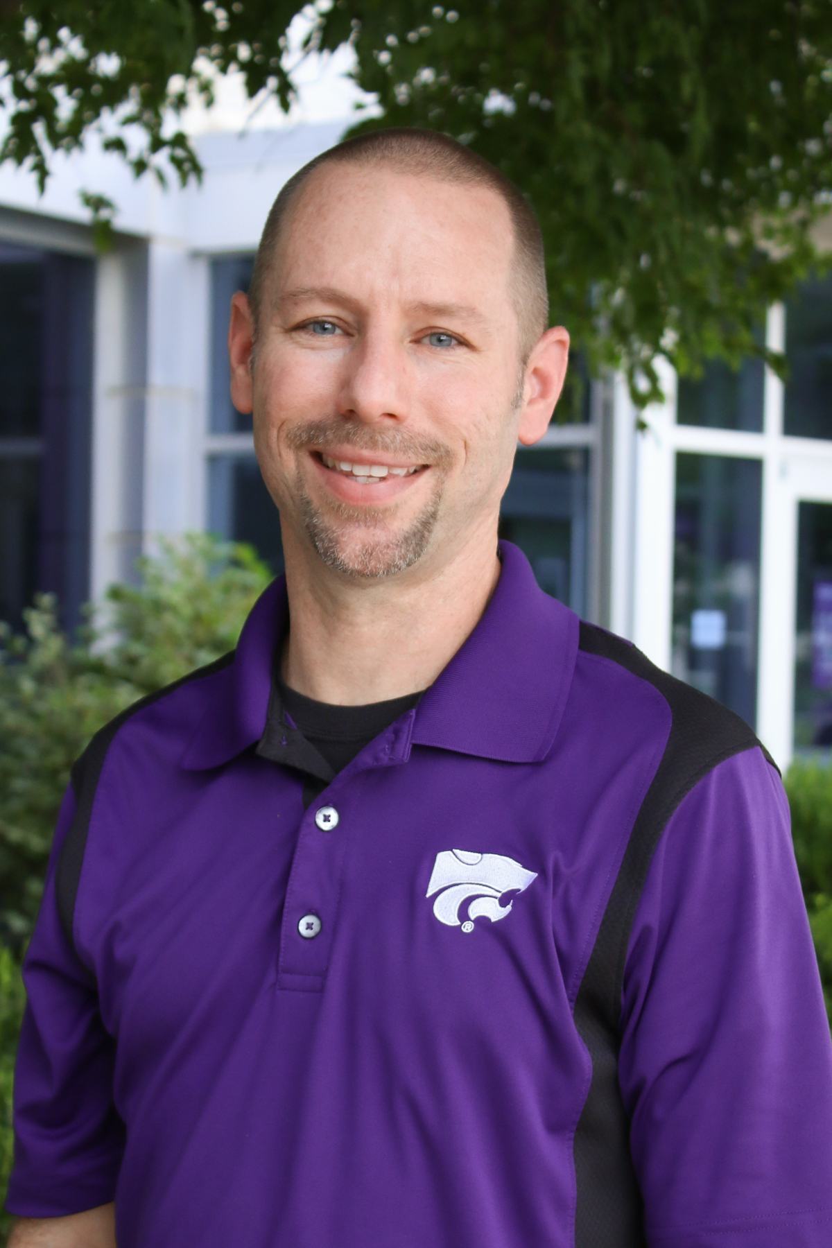 A white man in a purple polo with a white powercat logo smiles for a portrait photo.
