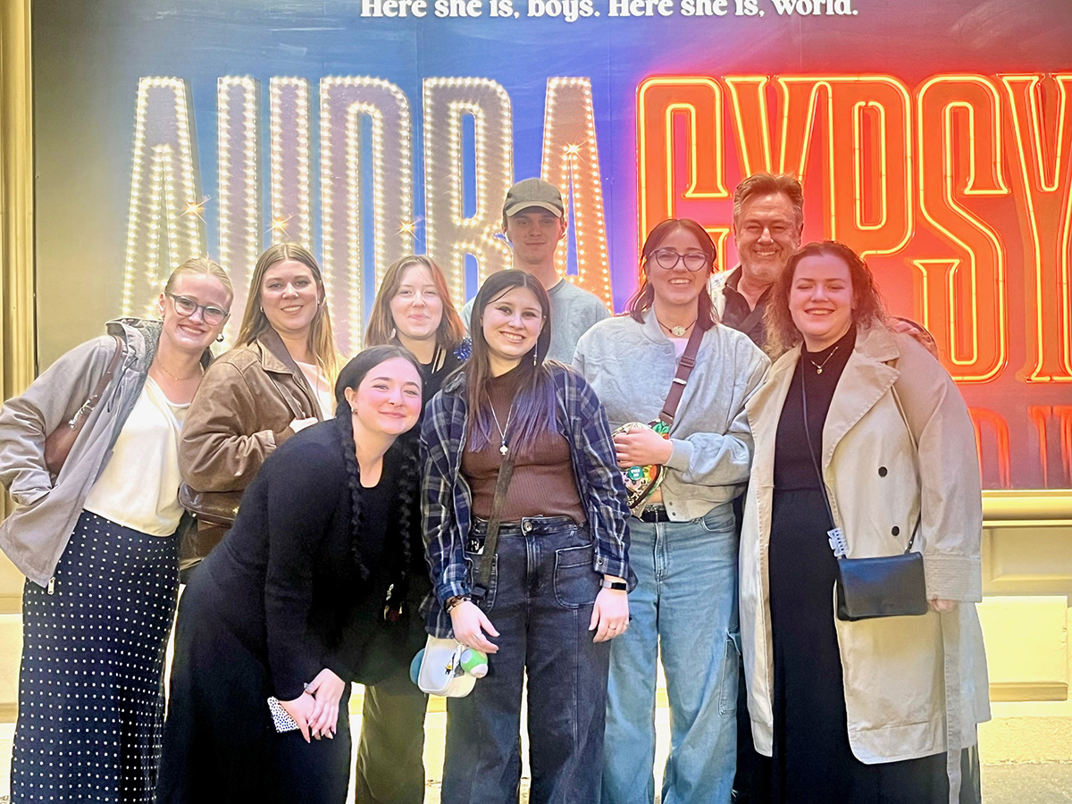 Group of nine people in front of a theatre sign.