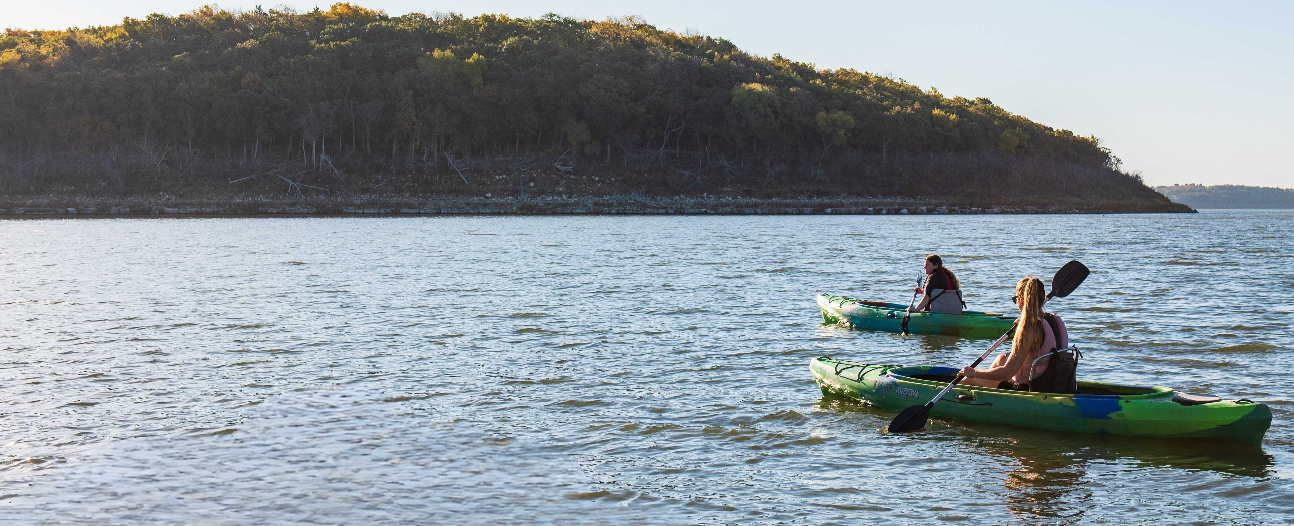 A couple of college students canoe away from the camera on a lake.