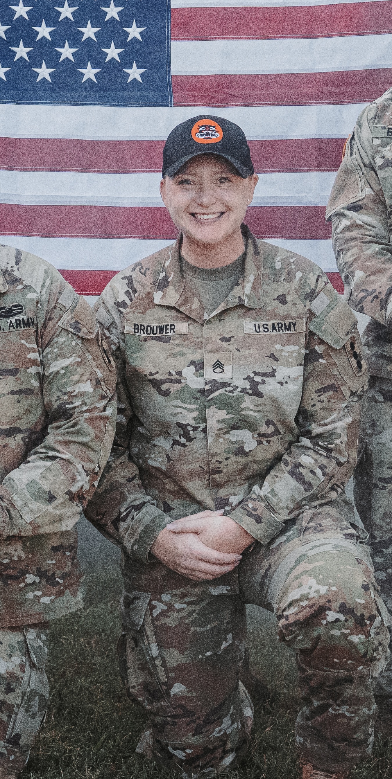 Hannah Brouwer A woman in an Army uniform smiling for a photo in front of the U.S. flag.