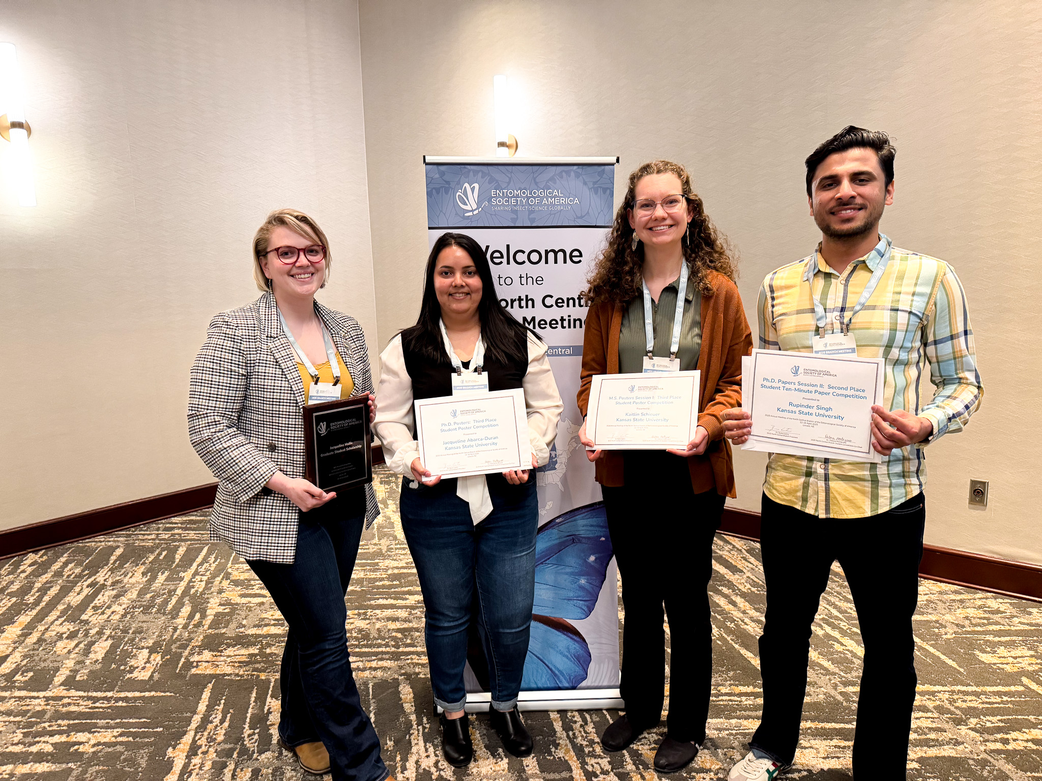 Four students stand with certificates in front of an Entomological Society of America banner.