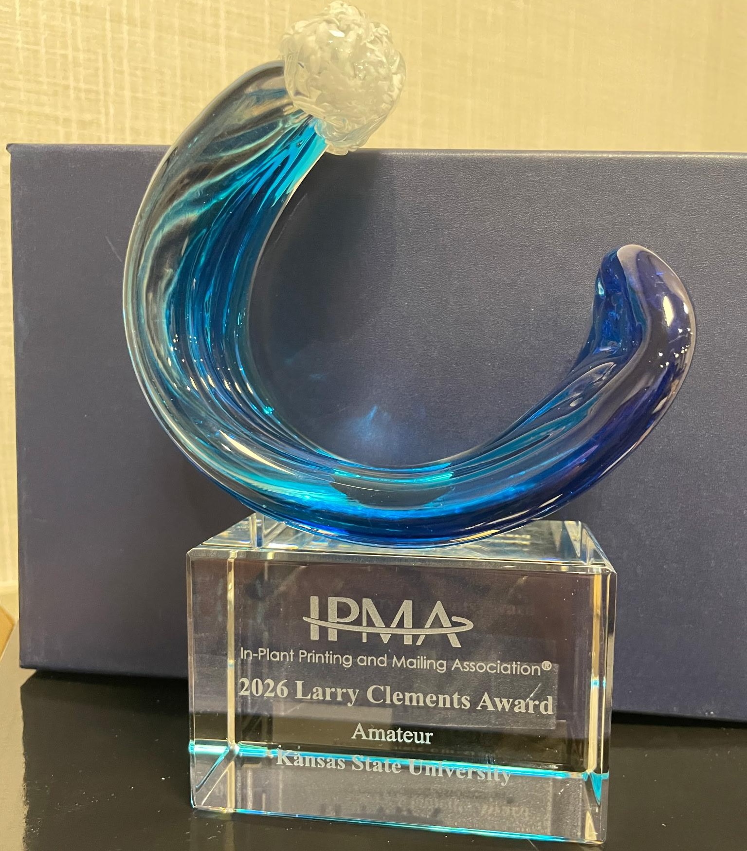 A glass award in the shape of a blue wave, with a commemorative plaque placed on the base