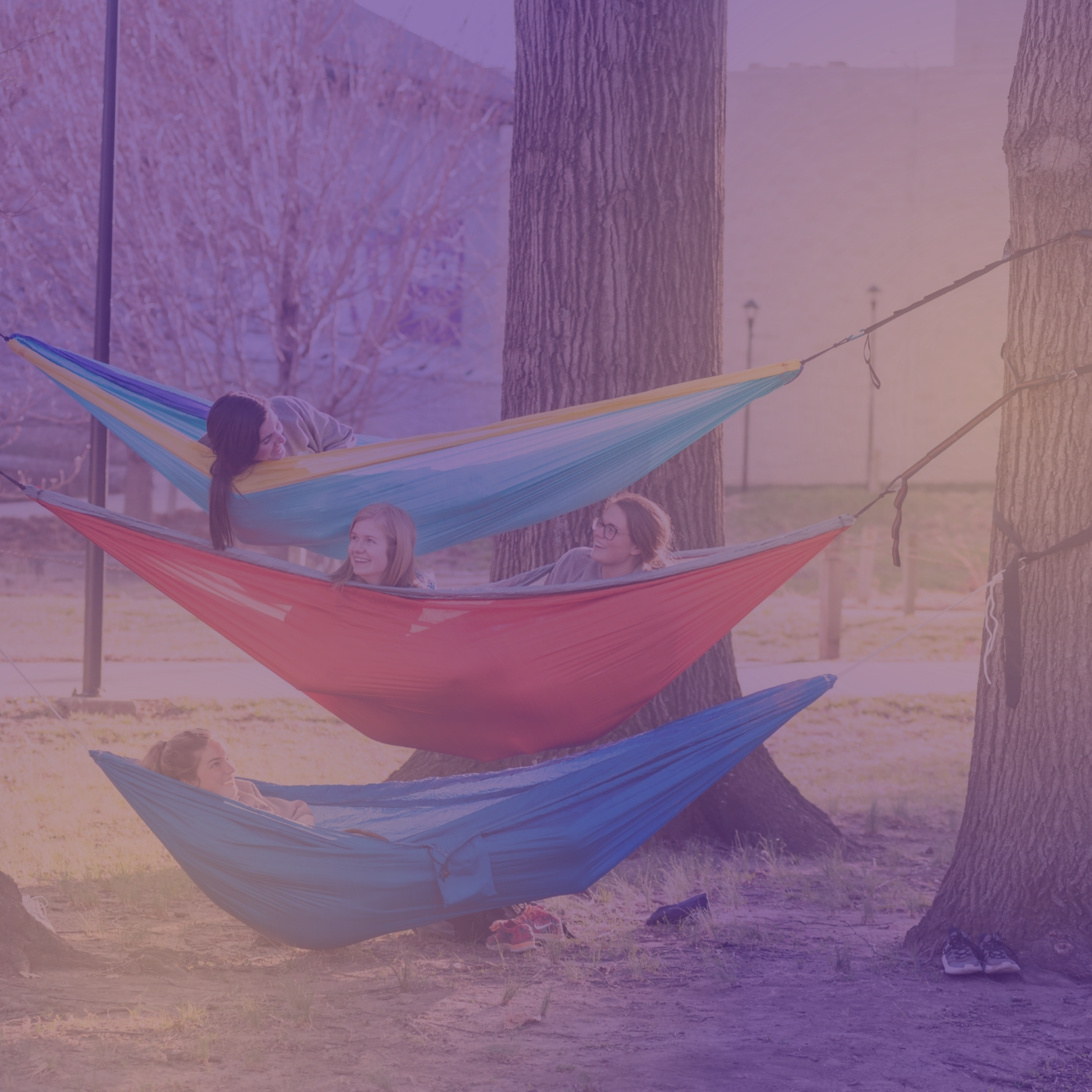 Four students lay on three stacked hammocks, laughing outside McCain Auditorium