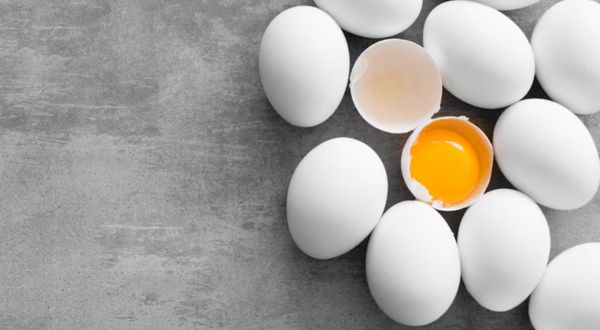 White eggs on concrete background, one open and showing yolk