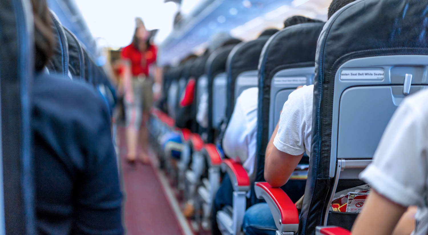 Blurred photo of airplane aisle facing the backs of the passengers.
