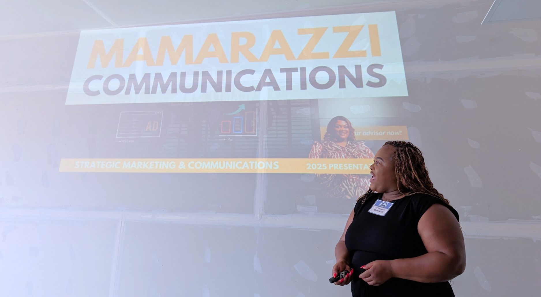 Woman speaking with a presentation clicker in front of a projector.